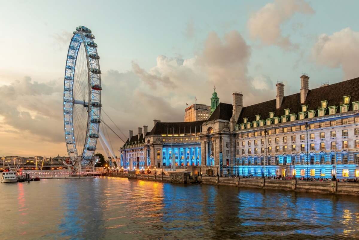 Ferris wheel and illuminated building by a river at dusk.