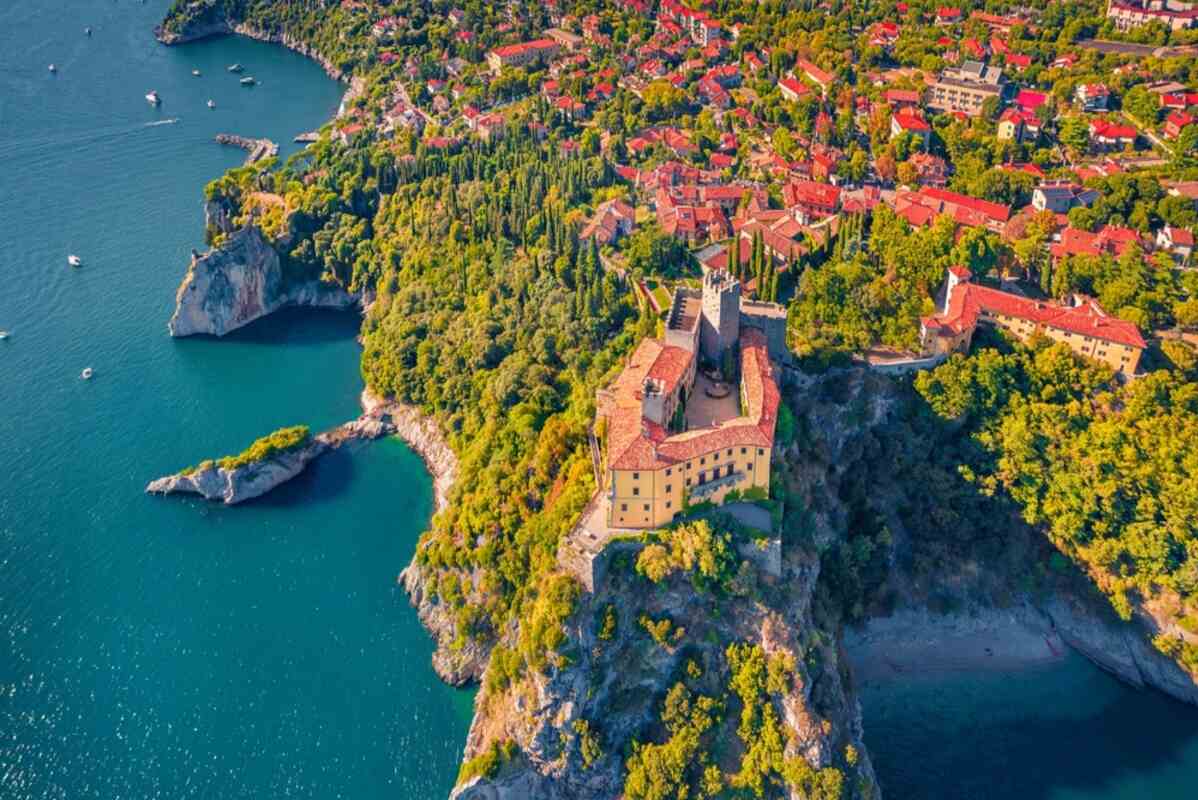 Yellow castle on a cliff overlooking the sea with boats and a town.