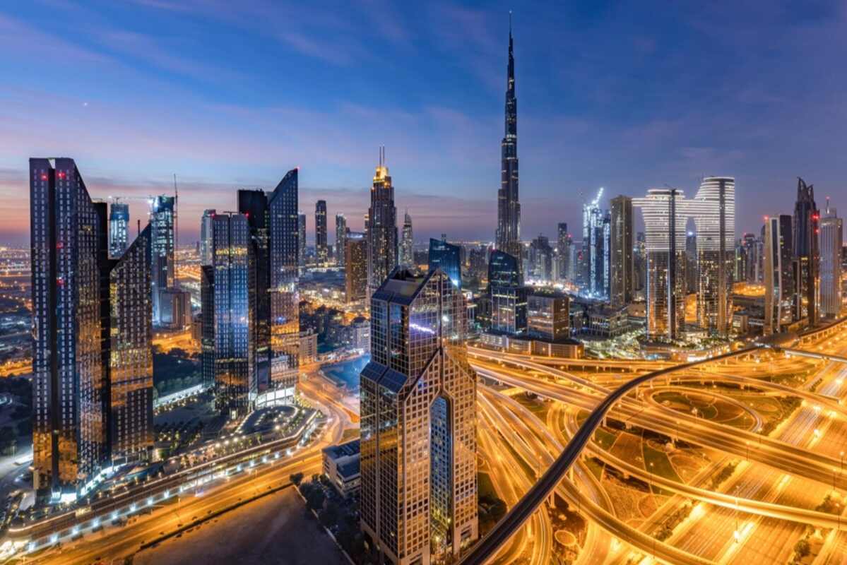 Twilight view of illuminated skyscrapers and highway interchange.