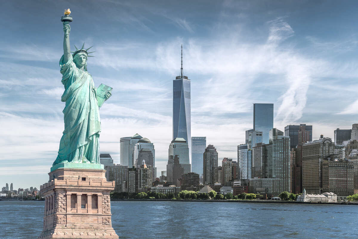 Statue holding a tablet overlooks a city skyline across the water.