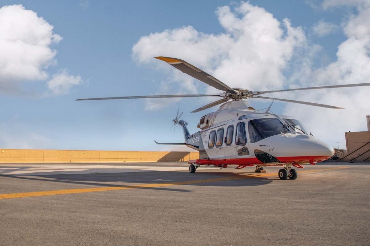 A white and red helicopter sits on a helipad, under a partly cloudy sky.