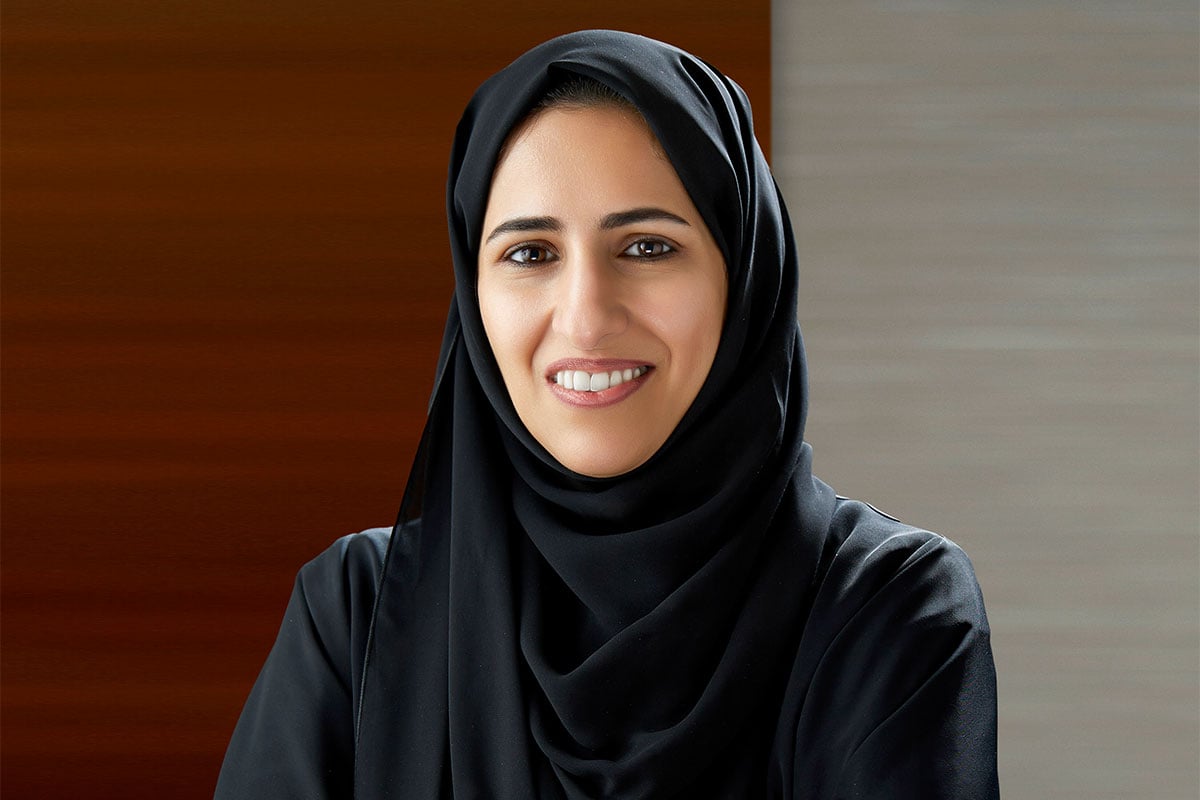 Woman in black hijab and abaya smiling against wood wall.