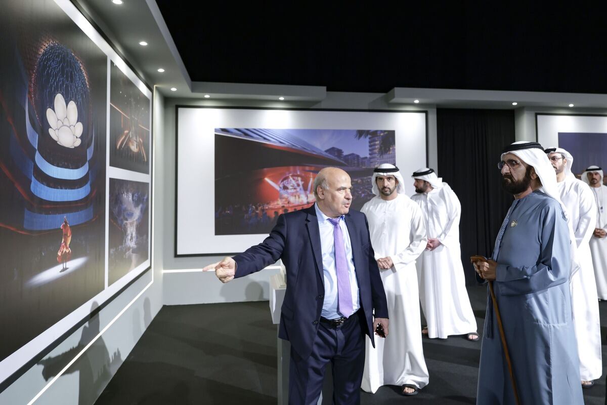 Man in suit points at architectural renderings with men in Emirati clothing.