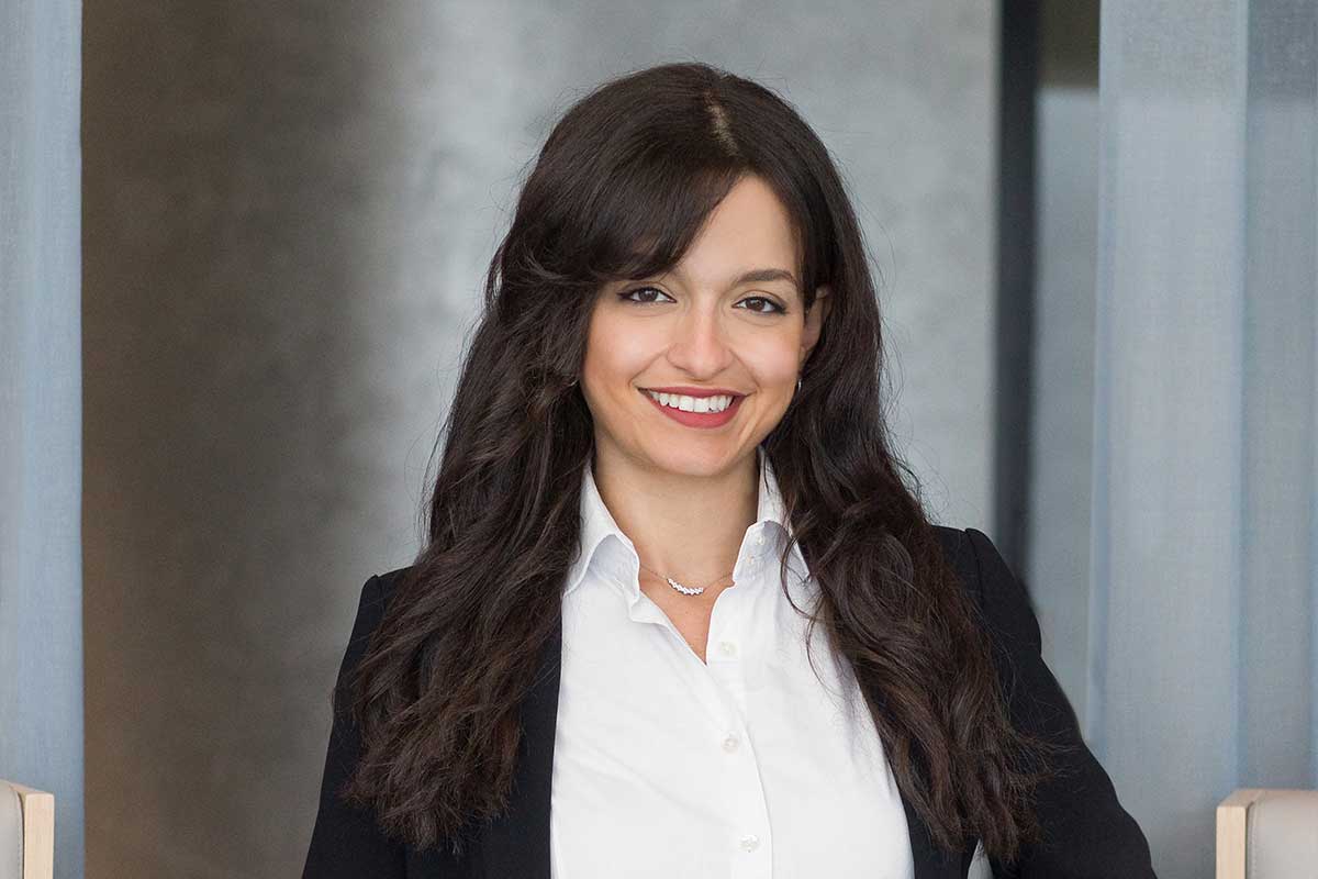 Woman in a black blazer smiling in a modern office.