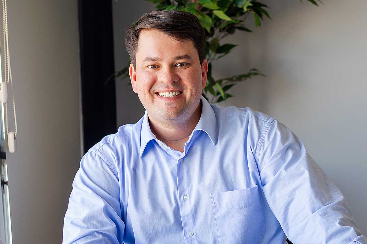 Man in light blue shirt smiles in office setting.