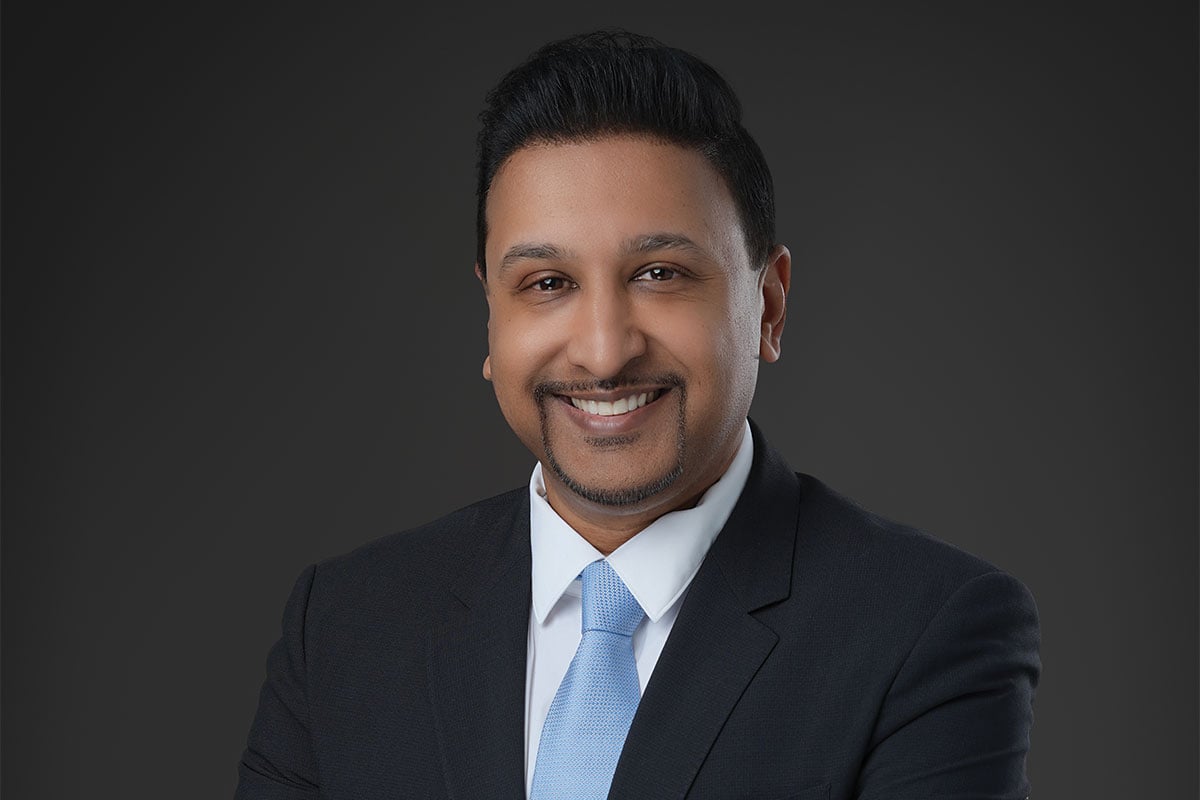 Smiling man in a dark suit and light blue tie.