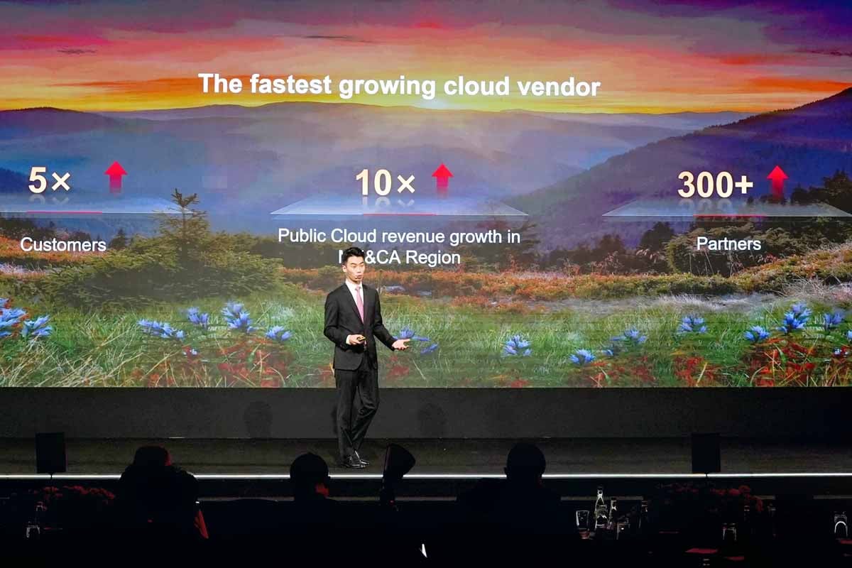 Man presents growth stats on a large screen in front of an audience.