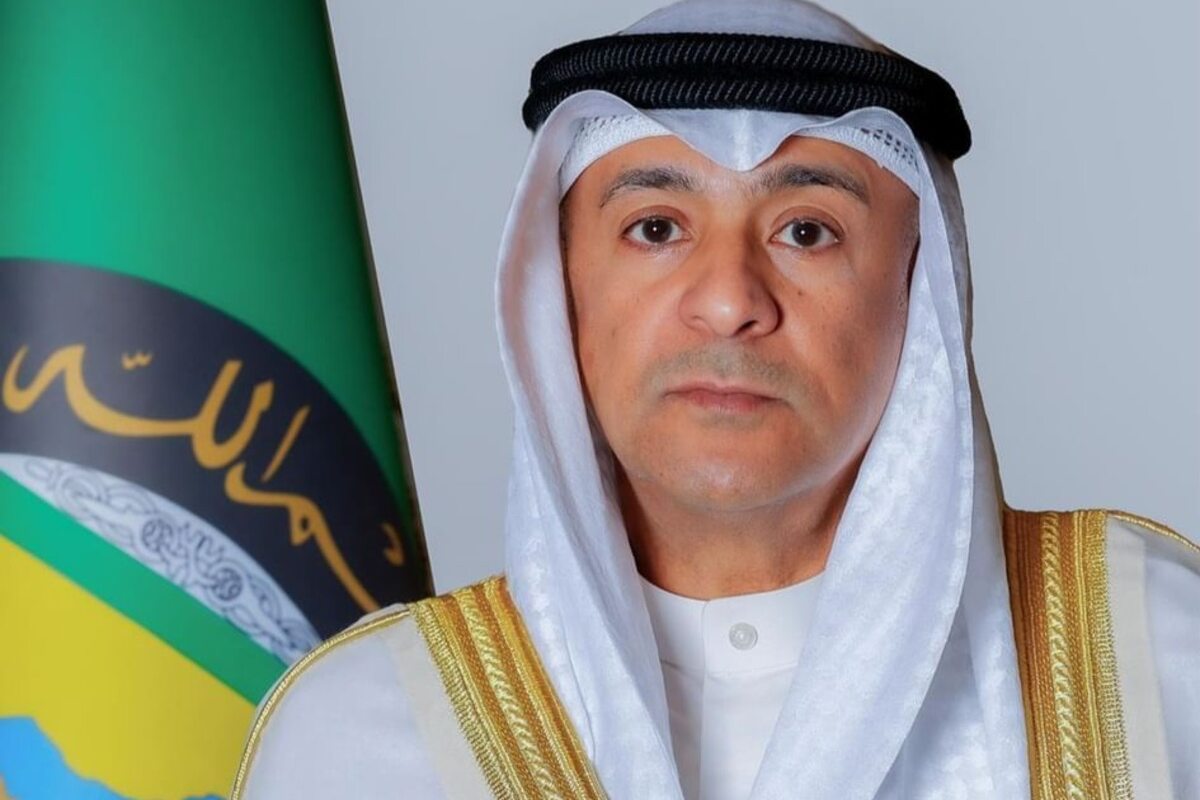 Man in Emirati attire posing against a flag with a serious expression.