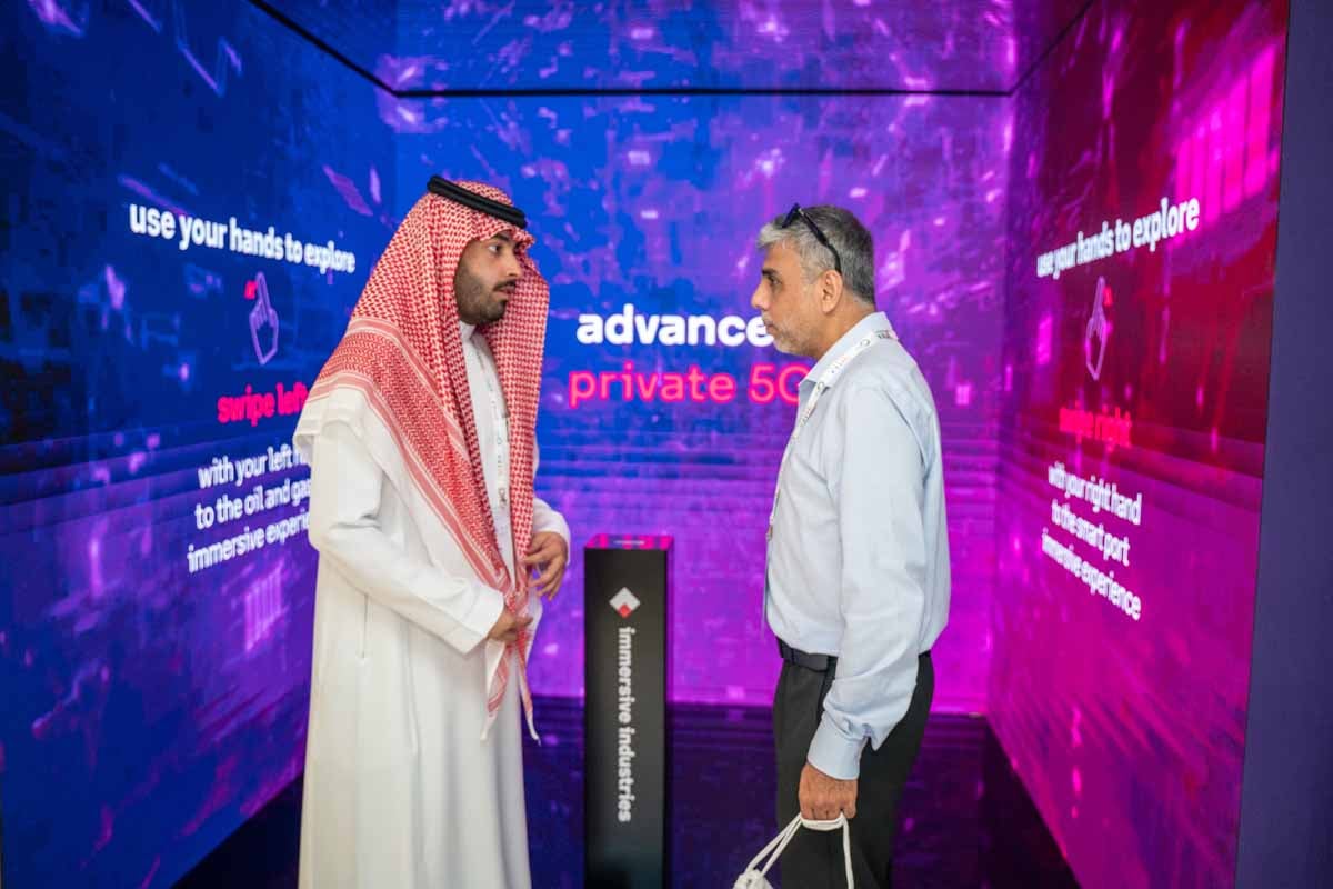 Two men discuss a private 5G display in Arabian and formal attire.