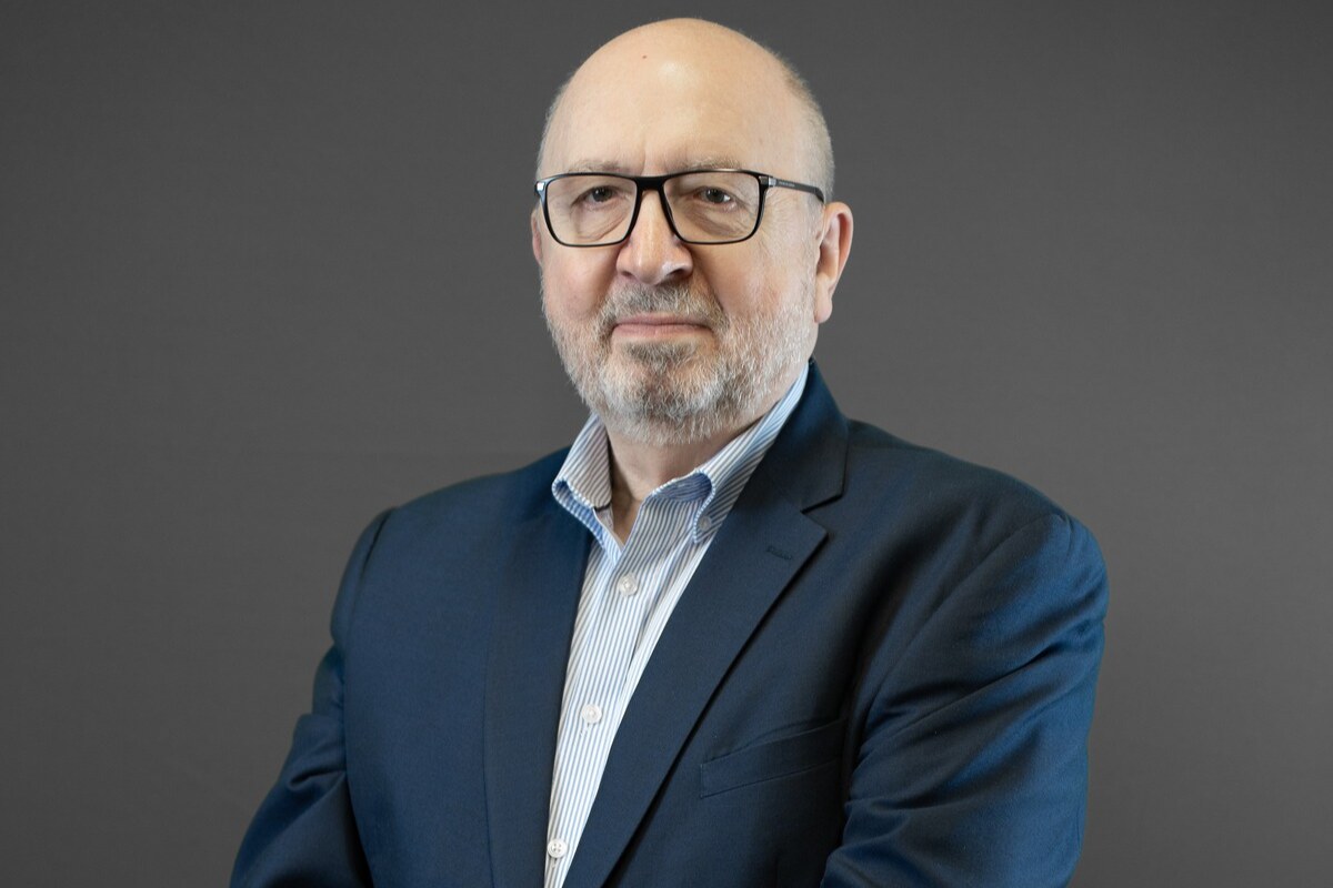 Bald man in a blue blazer against a gray background.