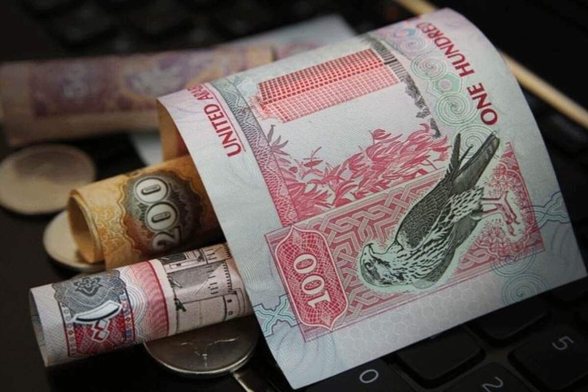 Rolled UAE dirhams on a keyboard with a prominent 100 dirham note.