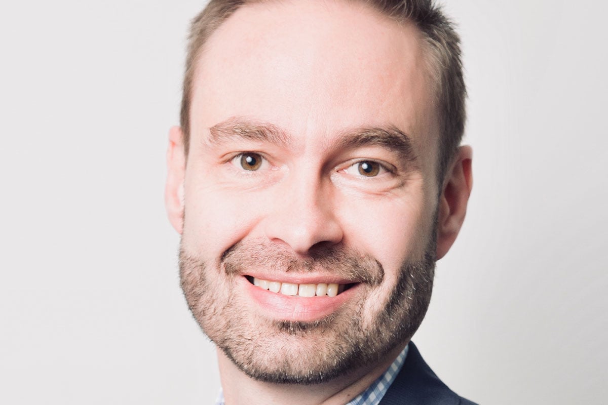 Man with a beard smiling against a light background.