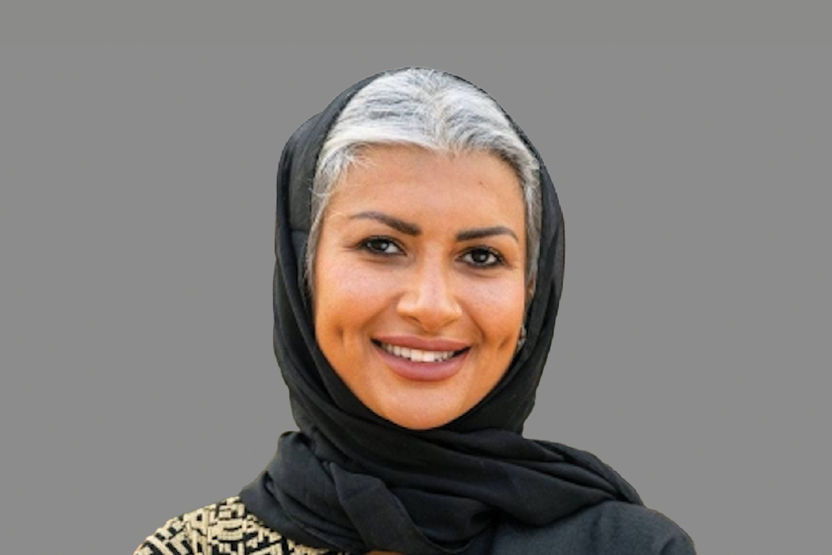 Woman in black headscarf smiles against gray background.