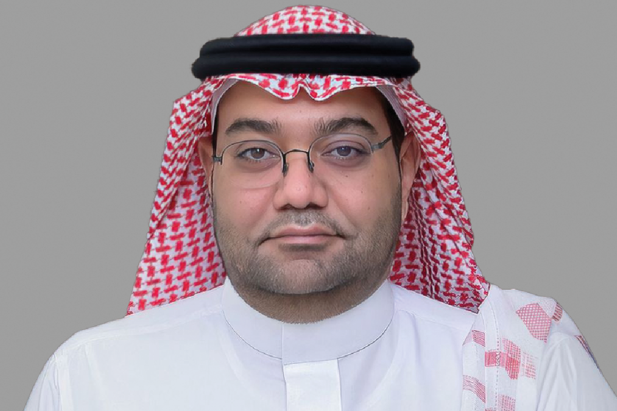 Man in red and white keffiyeh posing against a gray background.