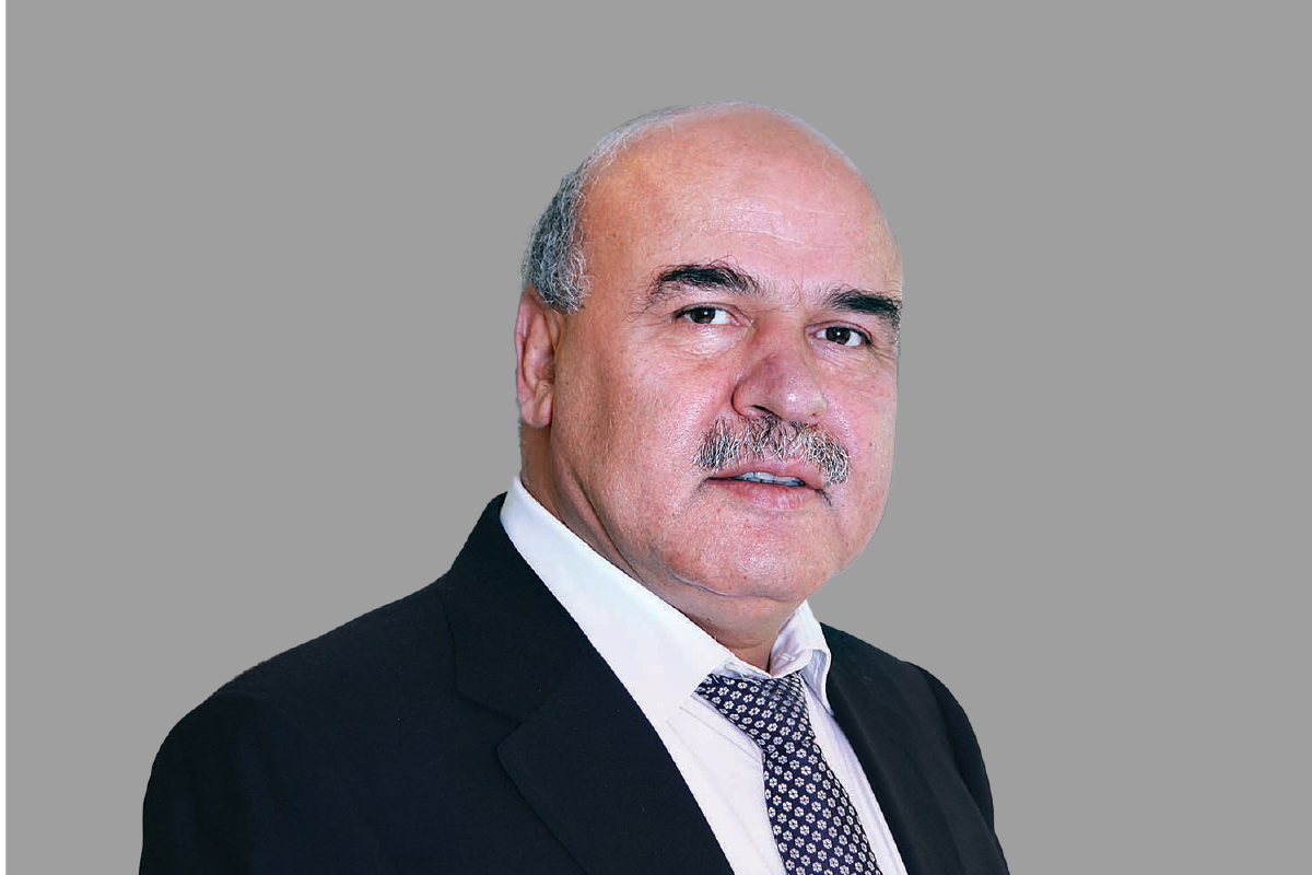 Bald man with a mustache posing in a suit against a gray background.