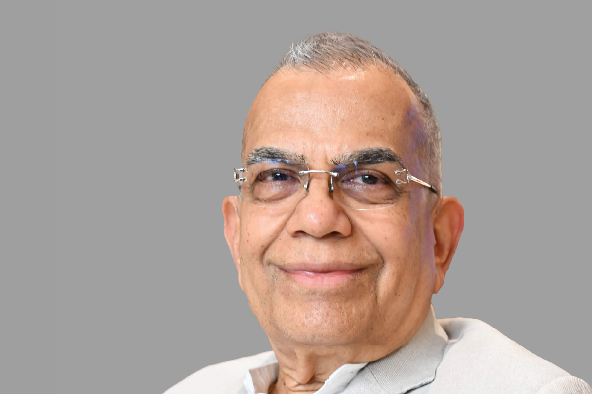 Man with glasses smiling against a gray background.
