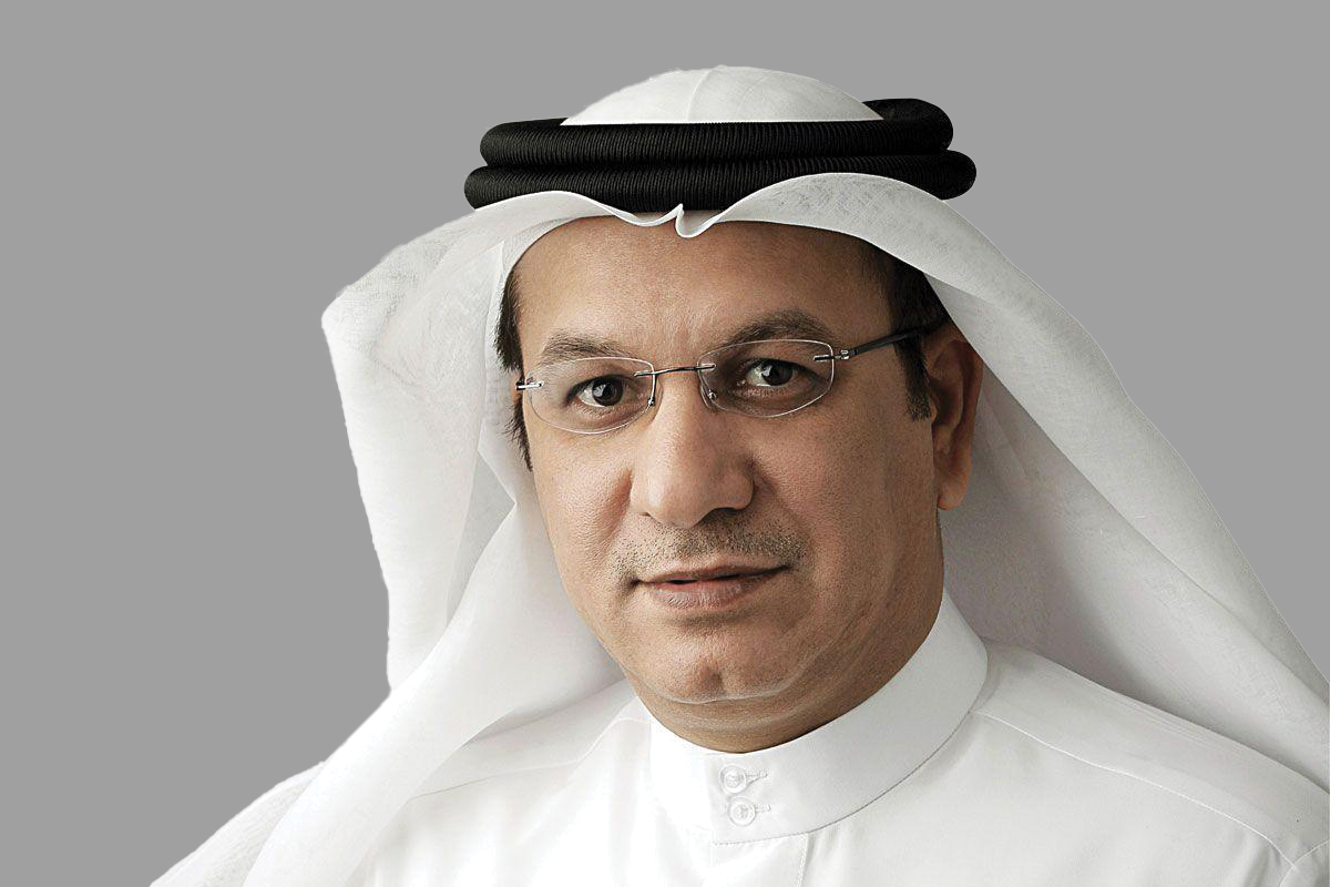 Man in glasses and Arab attire posing against gray.
